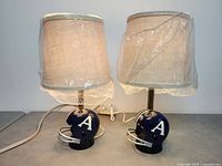 Two blue Toronto Argonauts CFL football helmet table lamps with beige fabric lampshades wrapped in plastic, showing front and side views.