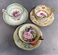 Three vintage teacup and saucer sets arranged to show floral designs and gold accents.