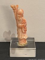 Front view of hand-carved salmon coral Guanyin figurine on clear acrylic base