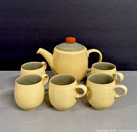 Set of one teapot with five matching mugs arranged together showing size and color contrast