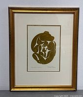 Framed gold embossed print with white matting and gold frame depicting Haida art style design of a bear and a human figure titled 'The Bear Mother'.