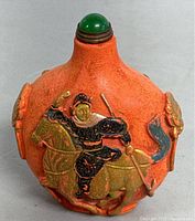 Close-up of the front of the red handmade Asian bottle featuring the detailed warrior on horse relief and green stopper.