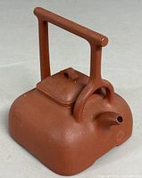 View of the traditional Chinese clay teapot showing the square base, handle, and spout from an angle.