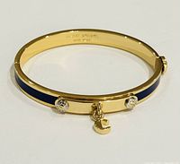 Front angle view of Henri Bendel gold-tone bangle bracelet with navy blue enamel and charm