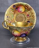 Front view of Aynsley teacup with hand-painted fruit and gold interior, saucer behind