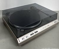 Photo of the closed turntable showing the tinted dust cover and front control panel with speed and start-stop buttons.