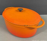 Side view showing the orange gradient color and two handles on the cast iron Dutch oven with minor enamel chipping on edges.
