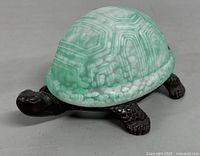 Front angled view of turtle lamp showing dark brown textured body and green glass shell.