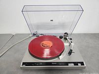 Top-down view of turntable on gray surface, dust cover open, red record on platter