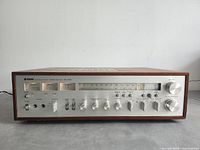 Front view of receiver showing silver control panel with VU meters, tuner scale and knobs.