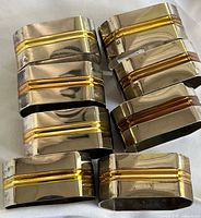 Group of eight silver napkin rings showing gold and copper accent stripes