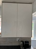 Front view of closed white high-gloss cabinet mounted on wall
