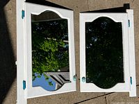 Both framed mirrors laid on pavement, showing white frames and blue hardware
