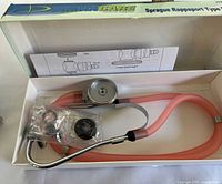 Opened box showing pink stethoscope, chestpiece, accessory bag and instructions