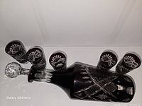 Decanter horizontal with stopper inserted, five shot glasses resting on decanter showing pattern and color