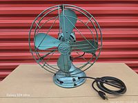 Full view of green four-blade desk fan with wire cage