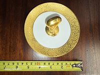 Top view showing gold encrusted rim, white center, gold handle, tape measure indicating diameter