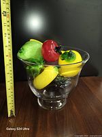Side view showing glass pedestal bowl filled with glass fruits