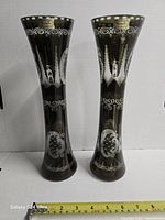 Front view of both olive crystal vases with tape measure for scale