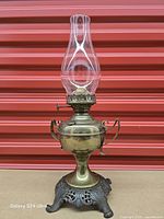 Full view of brass oil lamp assembled with glass chimney on cast iron base
