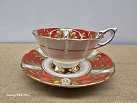 Side view of teacup on saucer showing red, white and gold gilt pattern