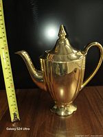 Front view of gold ceramic coffee pot with measuring tape for scale