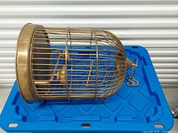 Side view of brass bird cage lying horizontal showing bars, perch, cups, and base