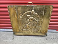 Front view of brass fireplace screen showing relief scene and feet