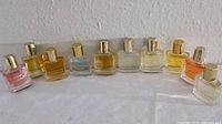 Line-up of ten square miniature perfume bottles showing varying liquid colors