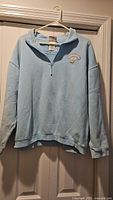 Full view of light blue quarter-zip Disneyland sweater on hanger