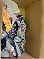 Box partially filled with patterned knit cardigan, orange top, others