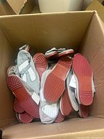 Box filled with grey canvas slip-on shoes showing red rubber outsoles