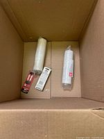 Bottom of box with two plastic wrap rolls, red tool and white packaged item