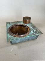 Top view of antique Japanese hibachi grill showing patinated brass surface, round coal holding opening, and cylindrical chimney with air holes