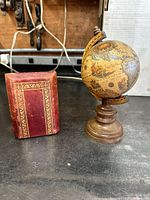 Both the antique Italian leatherbound book and the small vintage-style Italian globe on wooden pedestal stand placed side by side on a dark table surface.