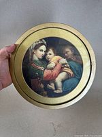 Full view of the round framed painting held in hand showing the religious figures inside the gold gilded frame.