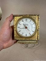 Front view of the gilded metal antique alarm clock showing dial and ornate engravings.