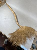 Full view of broom showing handmade curved wooden handle and fan-shaped straw bristles.