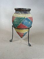 Front view of a small pottery amphora vase featuring multi-color Aztec geometric pattern on a metal stand.