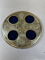 Top view of round brass coaster tray showing four circular blue felt inserts and pineapple embossed decoration.