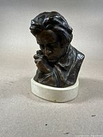 Front and side view of bronze bust statue showing facial features and detailed expression with head resting on hand.