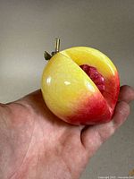 Photo of carved stone peach showing front and interior textured red detail, held in hand for scale