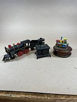 Overview photo of the cast iron train set, sample stove, and Swiss music box together on a plain surface.