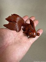 Rosewood carved goldfish figurine held in palm showcasing entire body, smooth polished finish and flowing tail and fins.