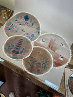 Four oval-shaped hand woven silk rugs laid overlapping on wooden floor. Each features distinct traditional Chinese designs and white fringed edges.