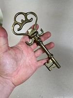 Brass giant skeleton key held in hand showing intricate bow design and solid shaft.