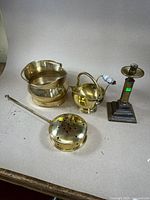 Five brassware items displayed on table: a heavy pot with handles, a steam warmer, a small covered pot, a candle holder and a crumber.