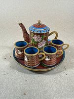 Side view of the cloisonné teapot, four cups, and round plate showing the detailed floral and bird enamel designs