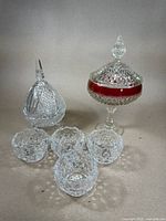 Group of crystal glassware including a lidded candy dish with red accent, lidded covered jar, and four small bowls