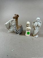 Four figurines including porcelain llama, white fish, resin girl with rabbit, and porcelain angel